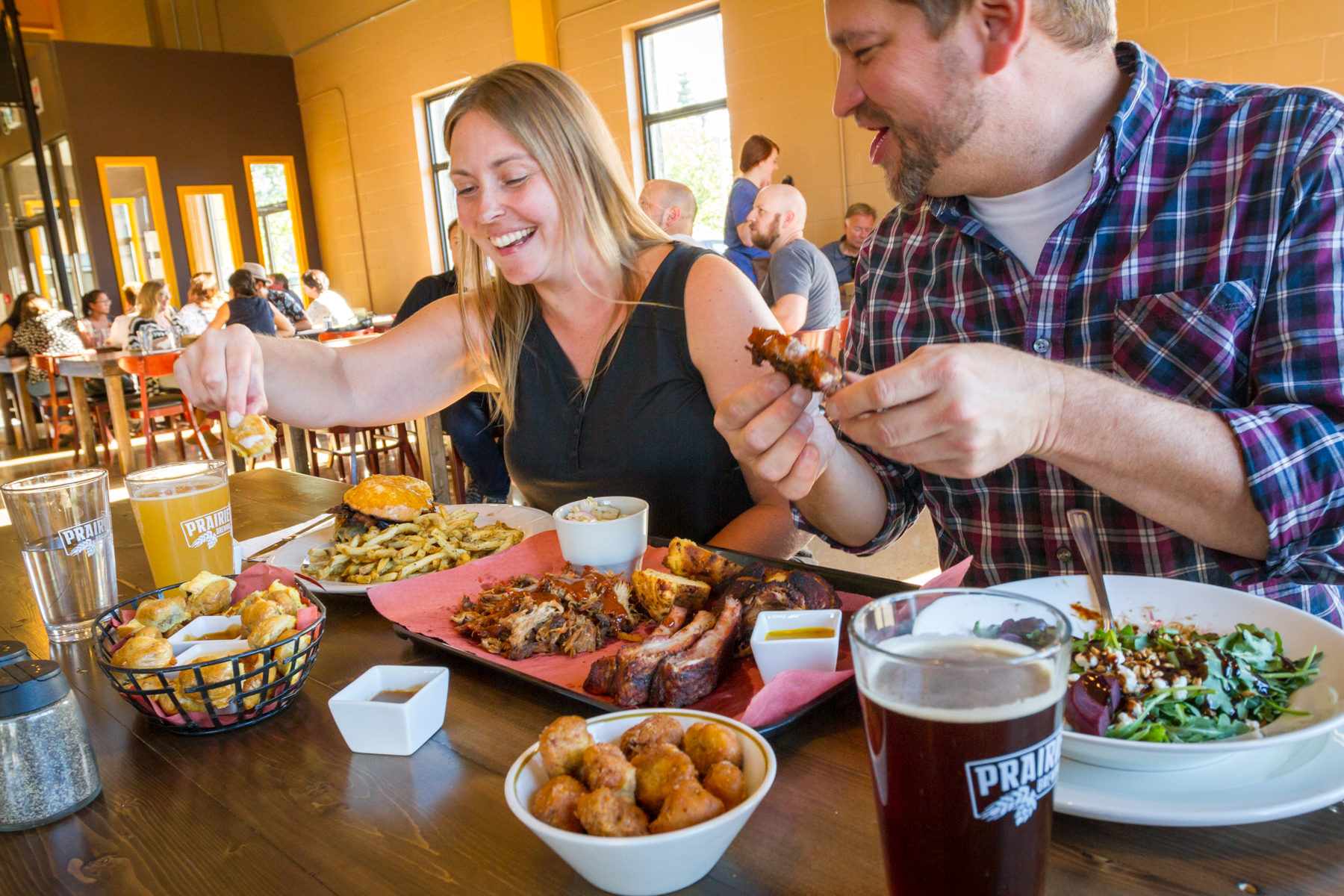 A couple eats Prairie Dog Brewing BBQ meats, salads and appetizers while drinking local craft beer.
