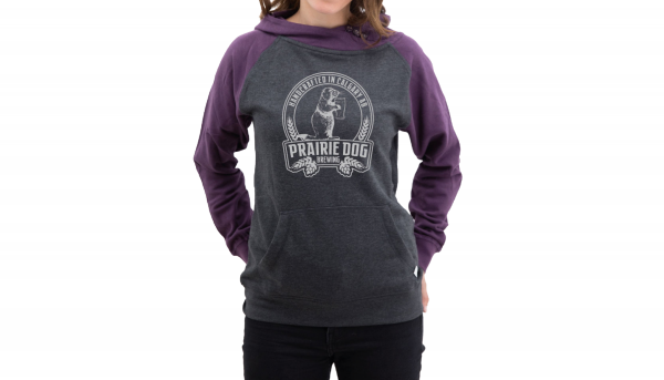 A woman wearing a hoodie with purple sleeves, a dark-grey torso with a light gray Prairie Dog Brewing badge on the front.