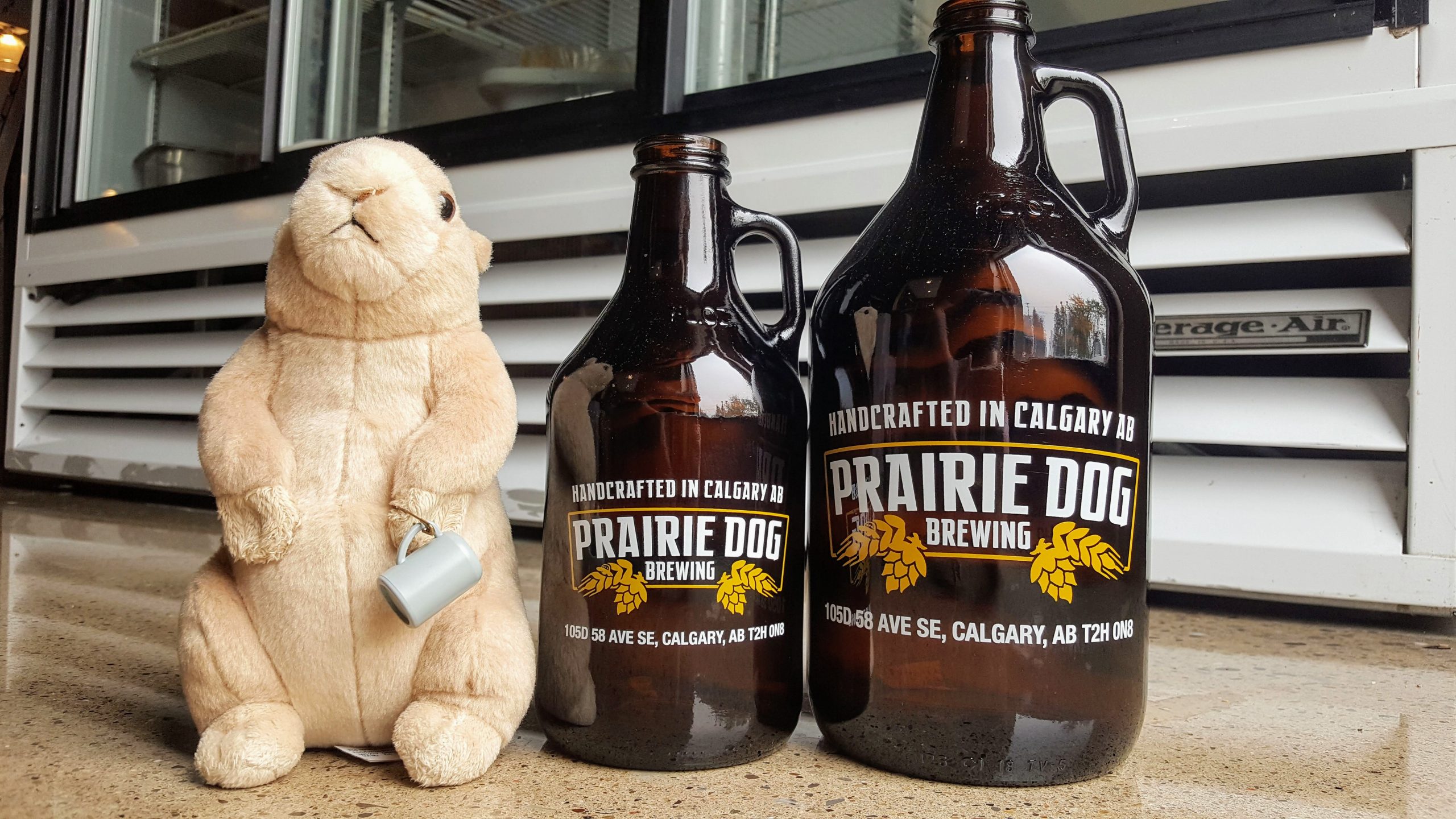 Prairie Dog howler jug and growler jug next to a prairie dog stuffed animal holding a beer stein.
