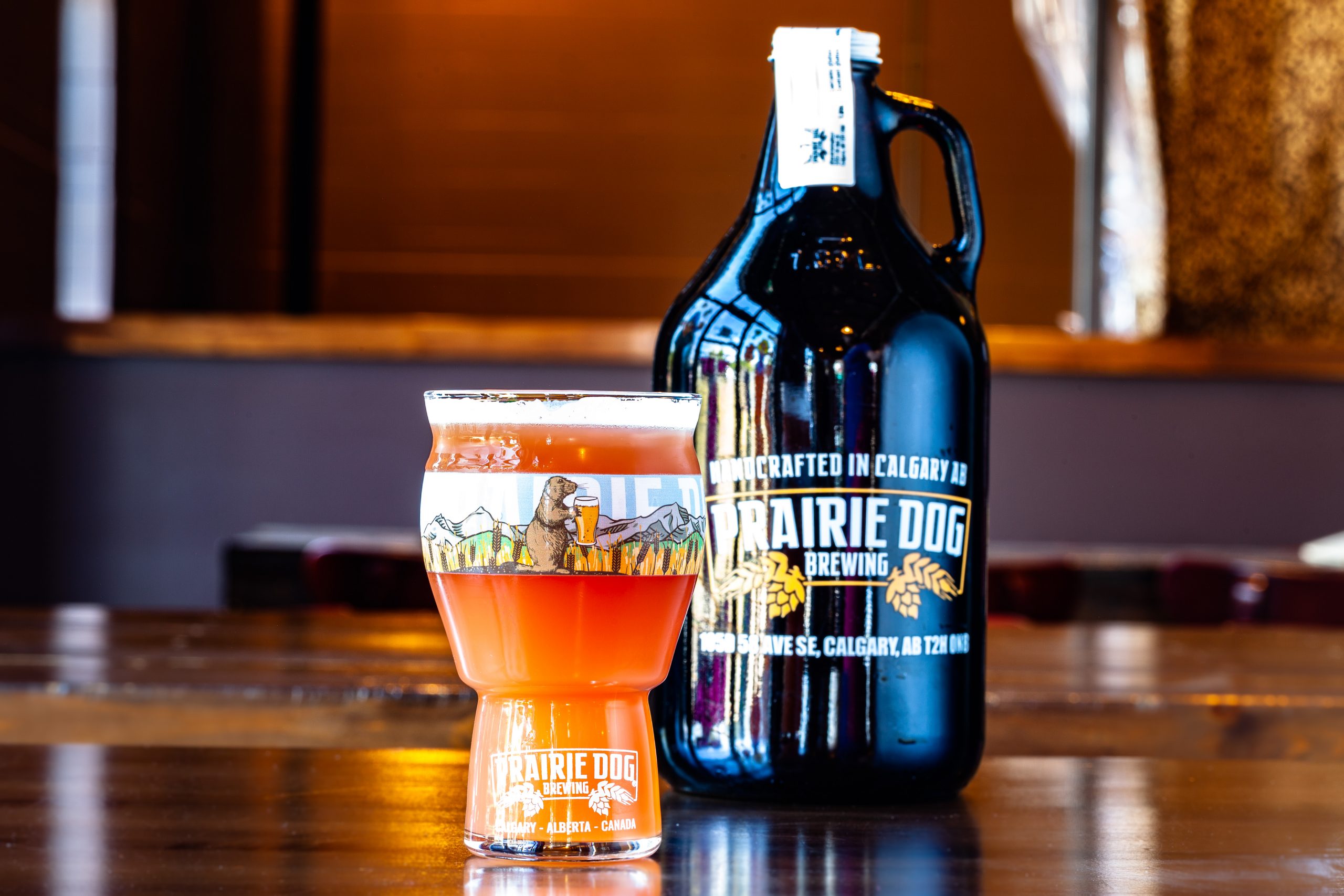 Prairie Dog Brewing Berry Burrow fruited Belgian-style blonde ale in a branded 16-oz US pint glass with a 64-oz branded growler in the background.