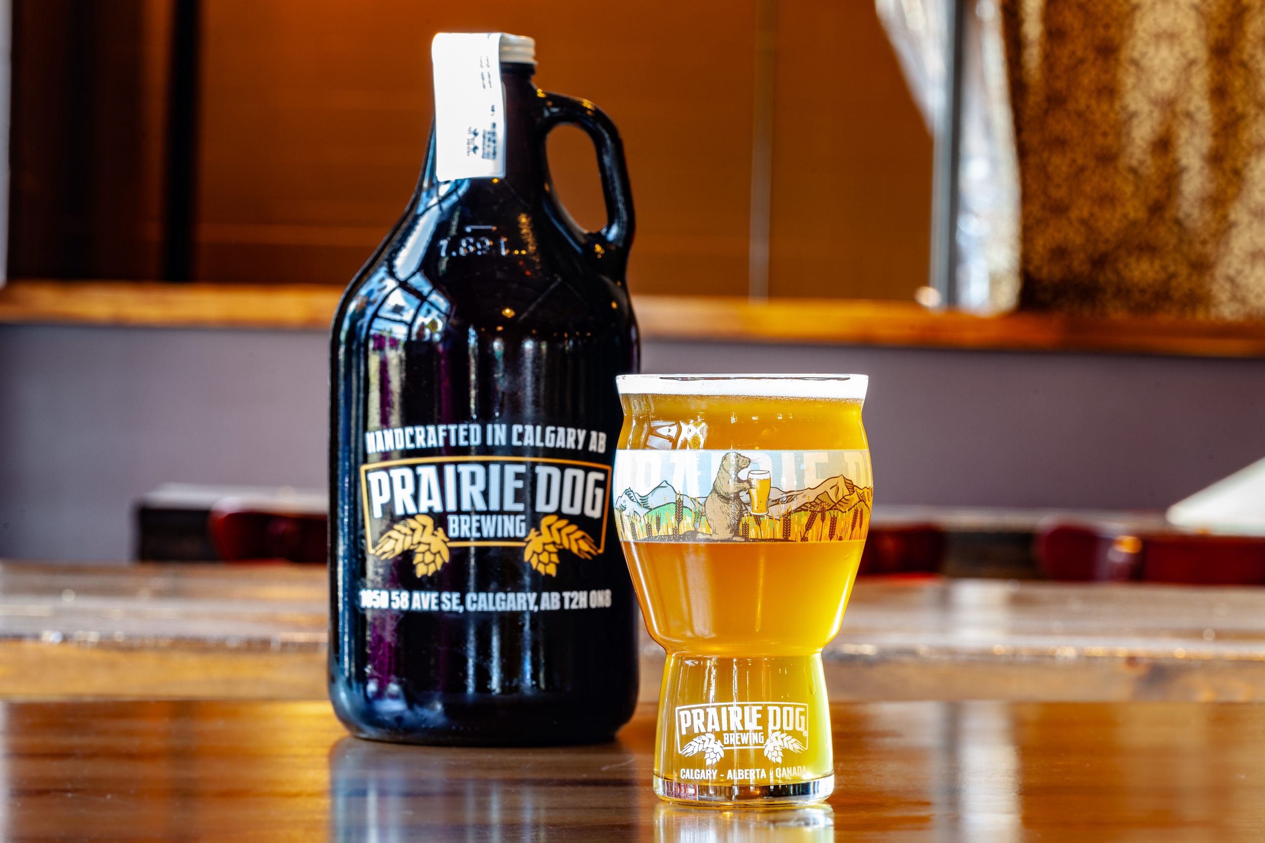 Prairie Dog Brewing's Ginger Lime Gose in a branded 16-oz US pint glass with a 64-oz branded growler jug in the background.