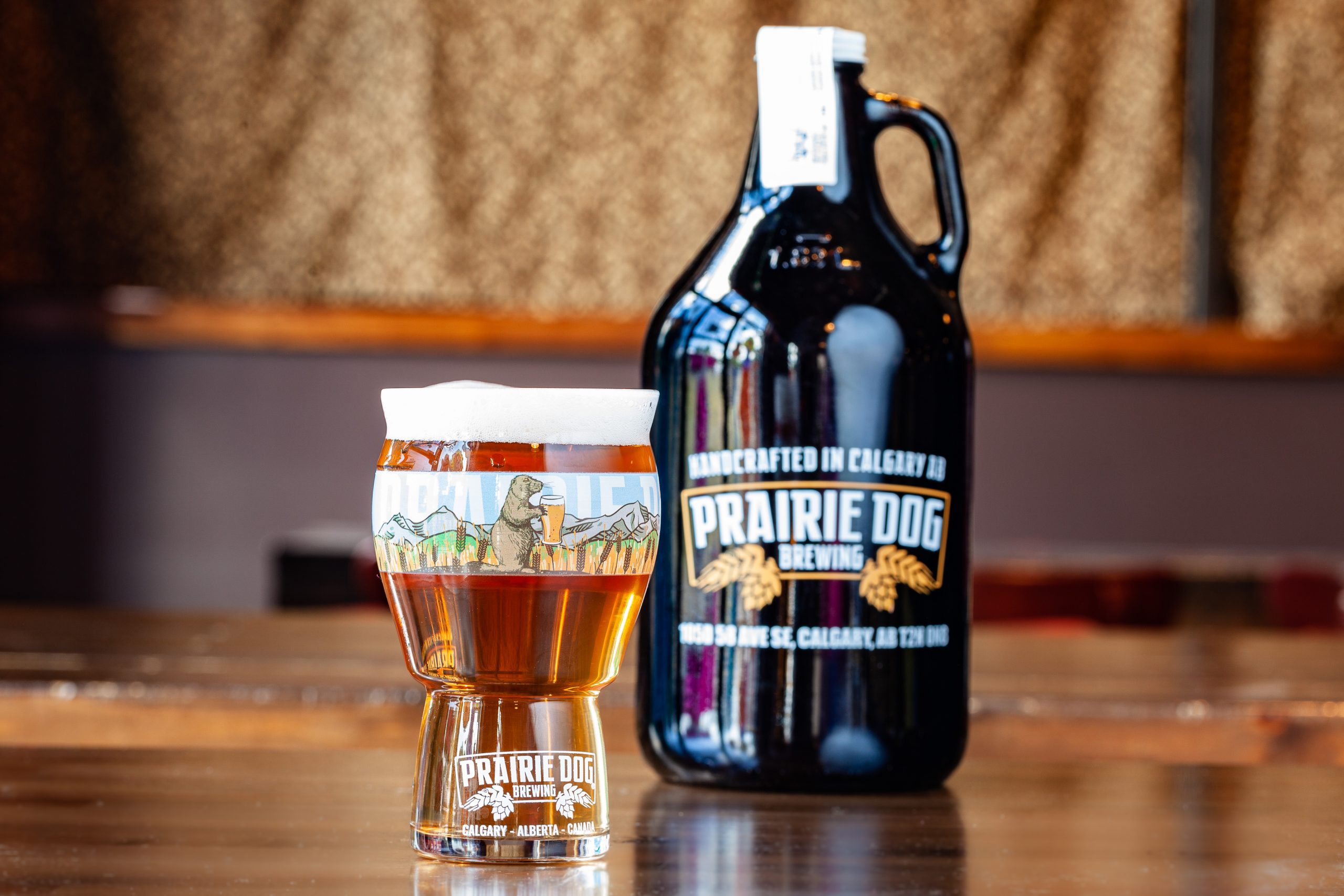 Prairie Dog Brewing's barrel-aged Kettle Sour Gone Wild! beer in a 16-oz branded pint glass with a 64-oz branded growler jug in the background.