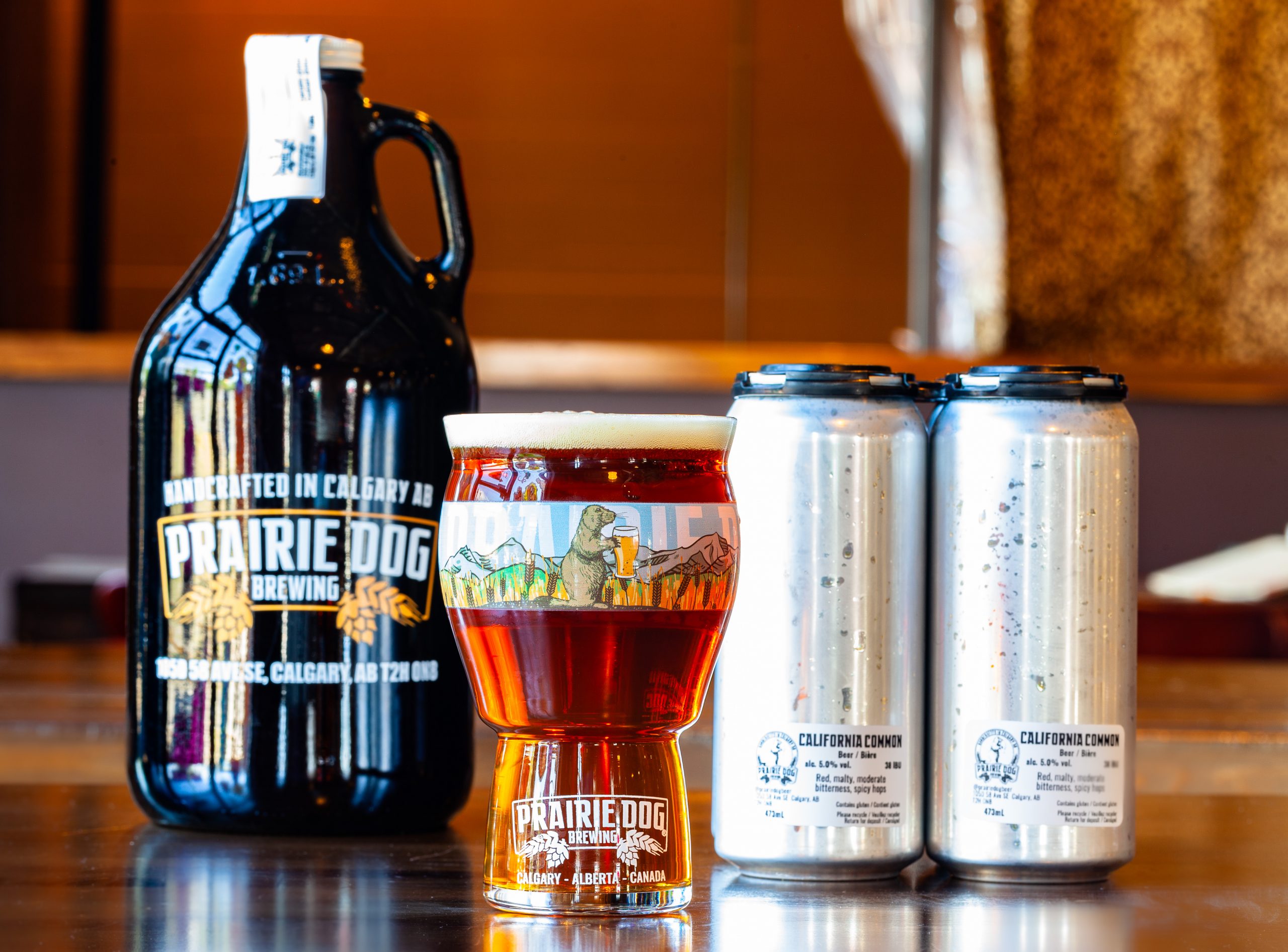 Prairie Dog Brewing's California Common red lager in a 16oz glass, 473mL cans and 64oz growler