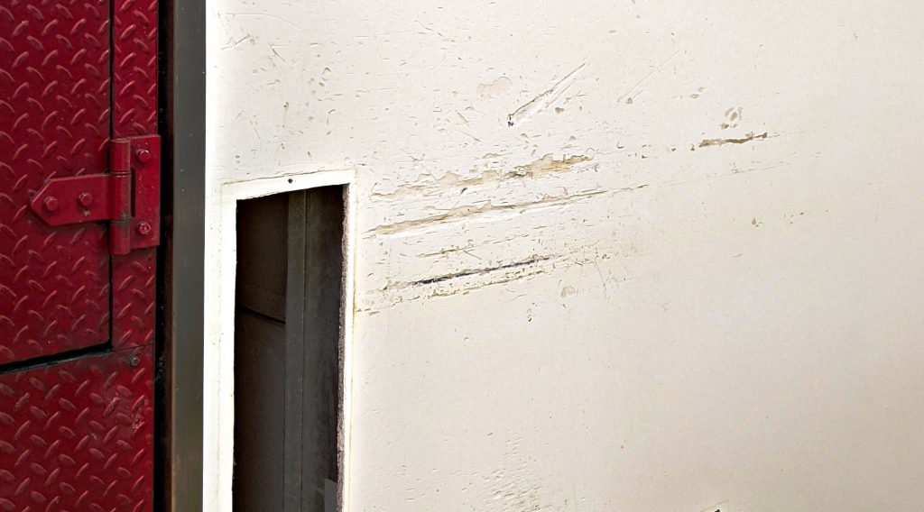 An image of painted drywall paneling in Prairie Dog Brewing's kitchen with substantial damage from repetitive impacts from kitchen equipment.