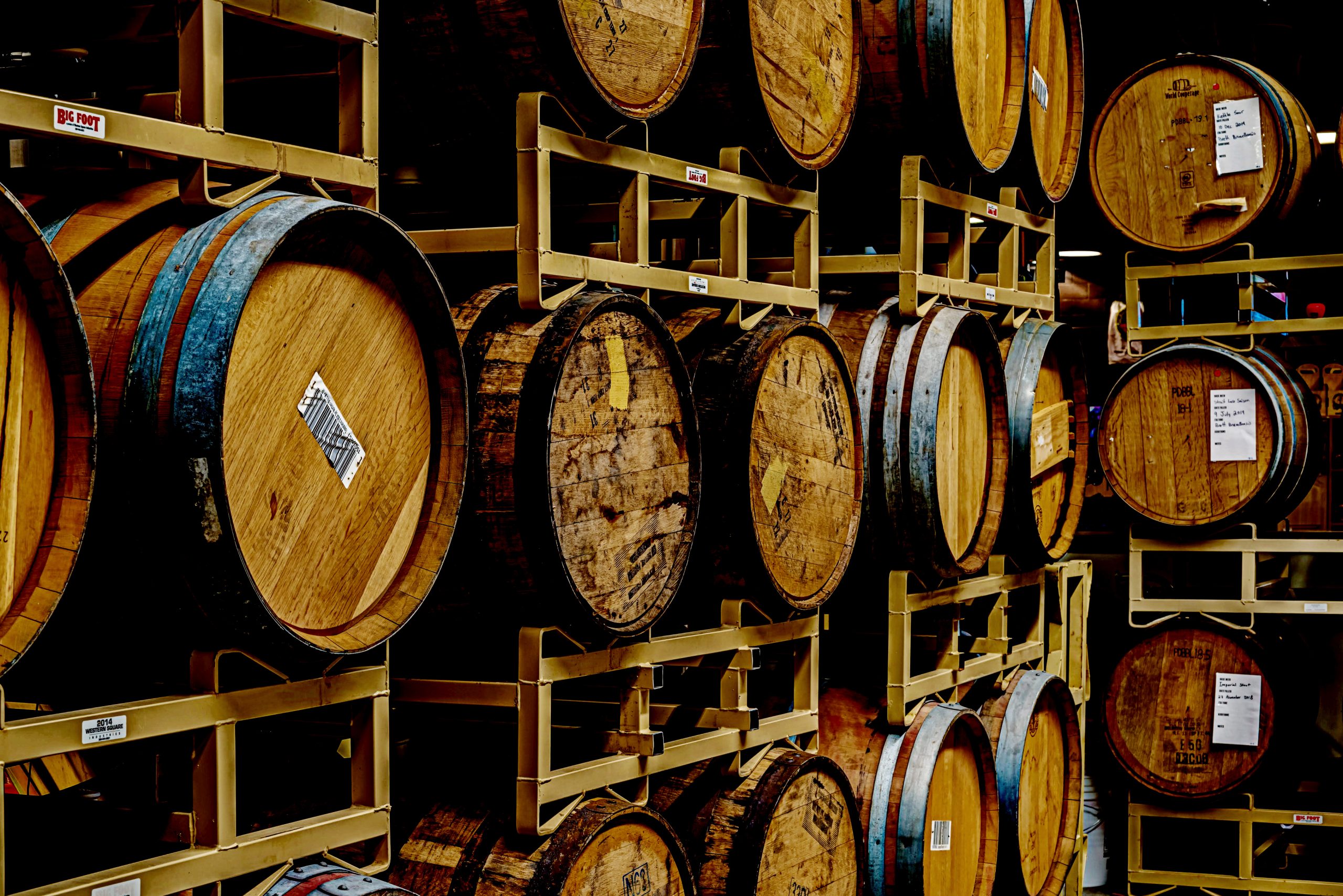 A dark, high-contrast image of oak whiskey and wine barrels stacked 3-high on racks at Prairie Dog Brewing.
