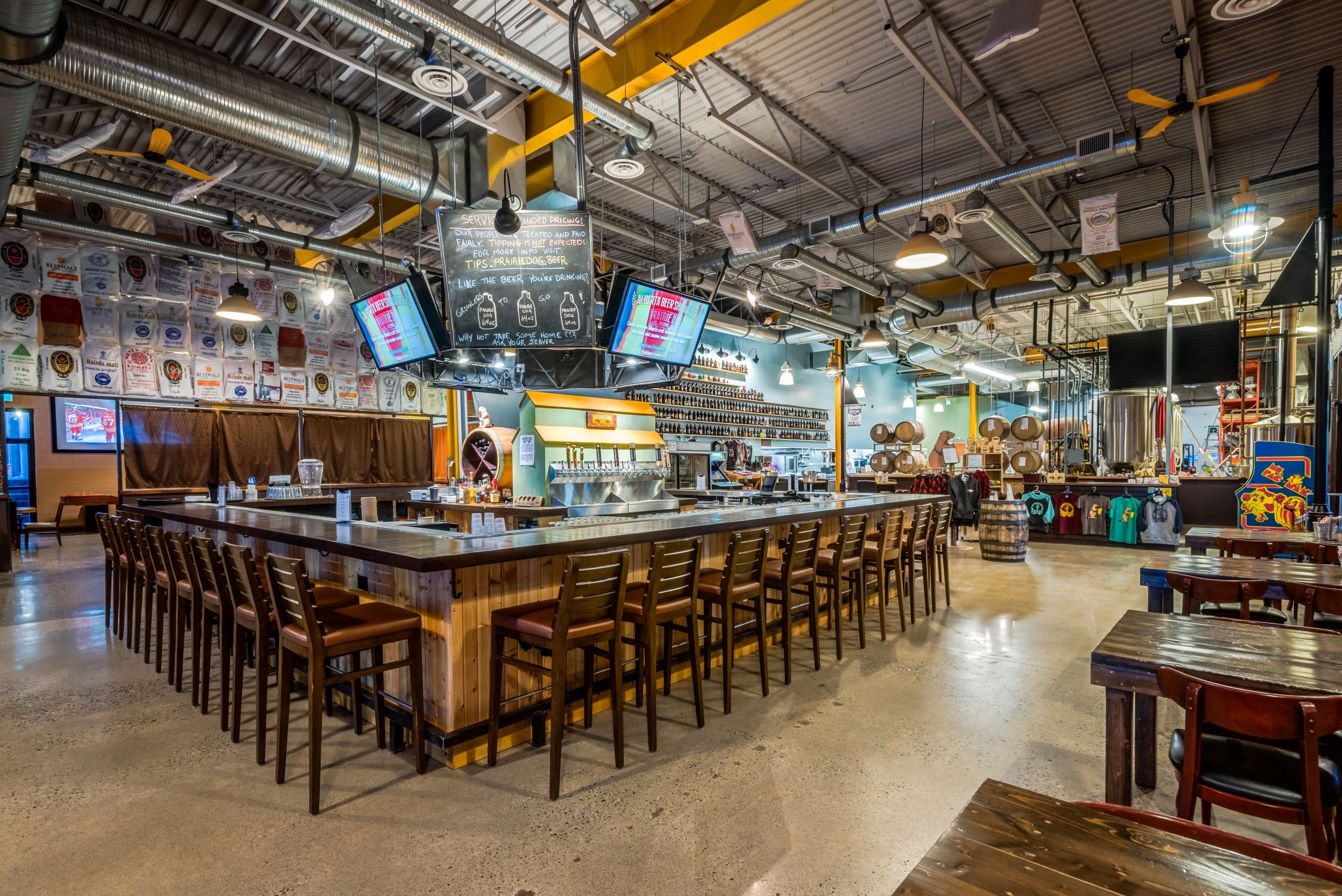 Prairie Dog Brewing's 58 Ave Location's beautiful wood bar centrepiece surrounded by empty chairs and an empty dining room.