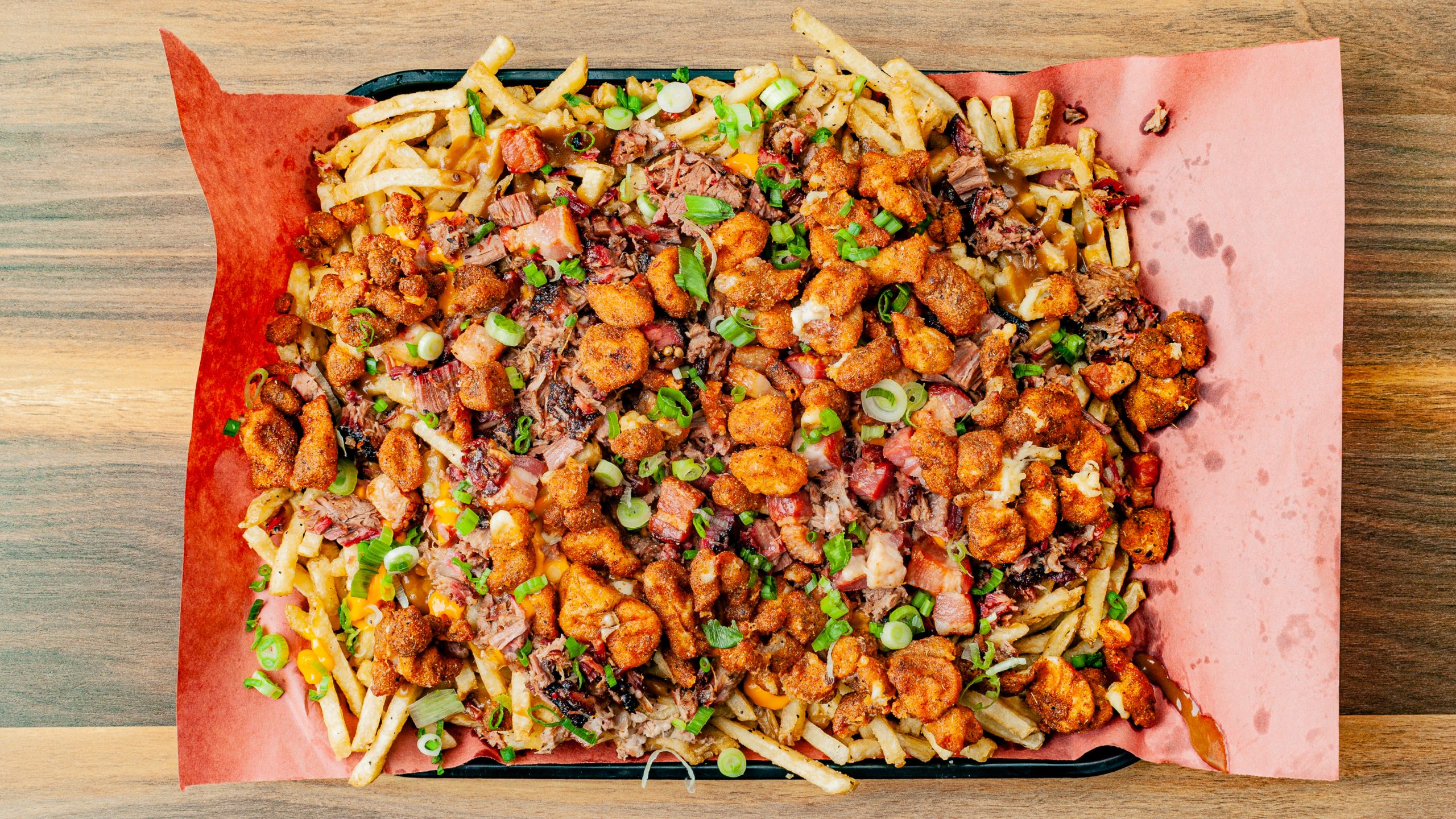 Prairie Dog Brewing's Extreme Poutine menu item, a platter with fries, gravy, nacho cheese, fried cheese curds, brisket, pulled pork, bacon lardons, and green onions.