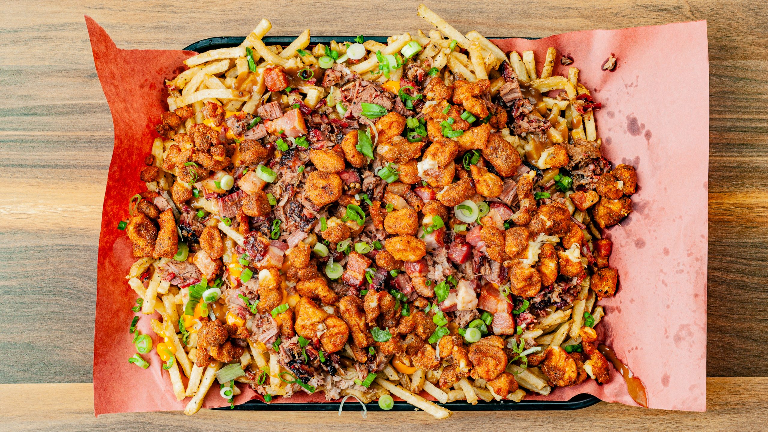 Prairie Dog Brewing Extreme Poutine Prairie Dog Brewing's Extreme Poutine menu item, a platter with fries, gravy, nacho cheese, fried cheese curds, brisket, pulled pork, bacon lardons, and green onions.