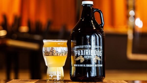 A 64-oz growler jug alongside a 16-oz pint of Prairie Dog Brewing's refreshing and straw-coloured Strait-Laced Saison.