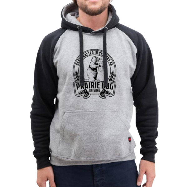 A man wearing a hoodie with black sleeves and a light gray torso with the Prairie Dog Brewing badge in black on the front.