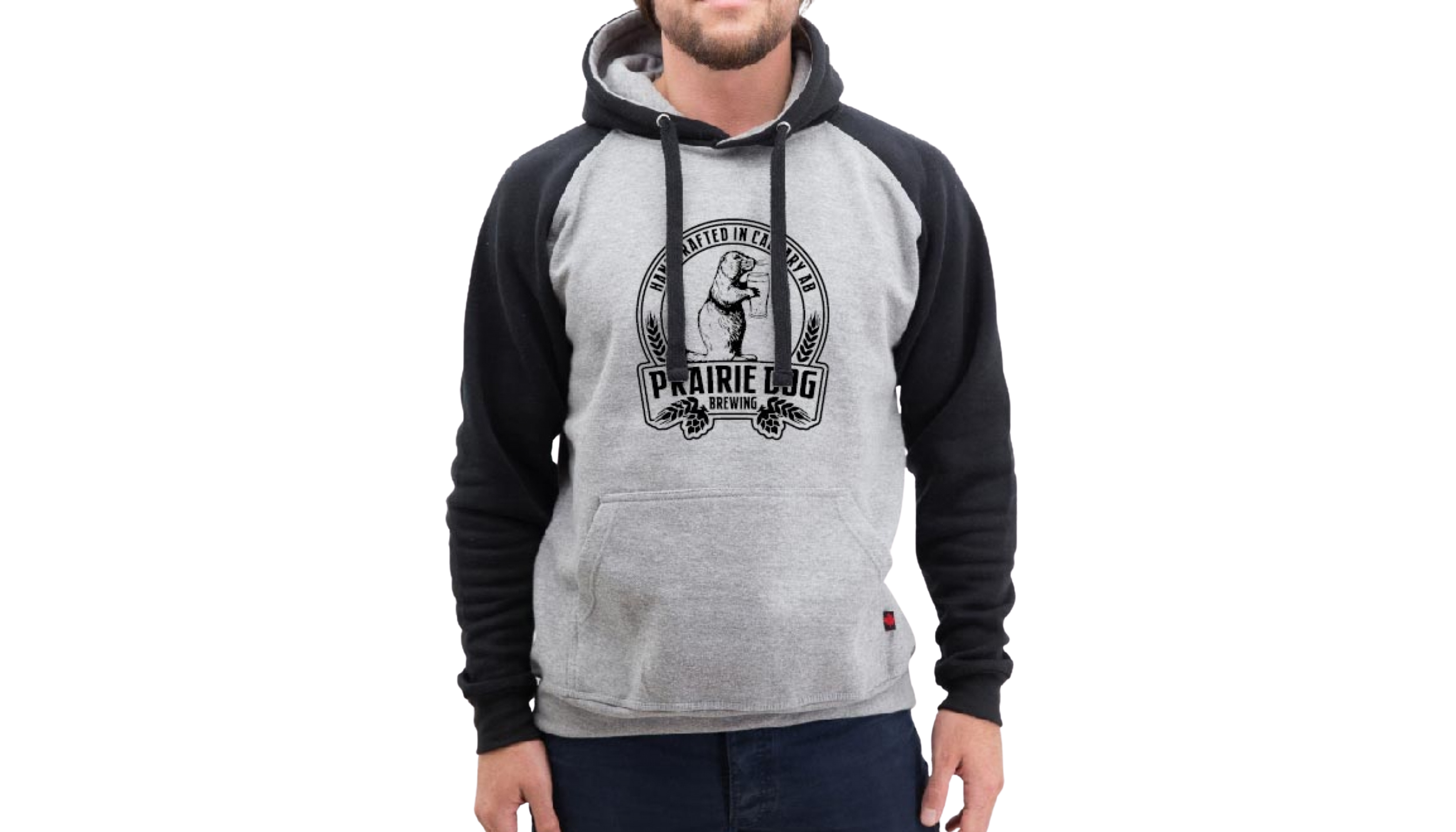 A man wearing a hoodie with black sleeves and a light gray torso with the Prairie Dog Brewing badge in black on the front.