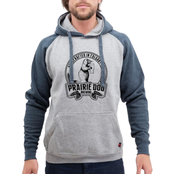 A man wearing a hoodie with denim coloured sleeves and a grey torso with the Prairie Dog Brewing badge in black on the front.