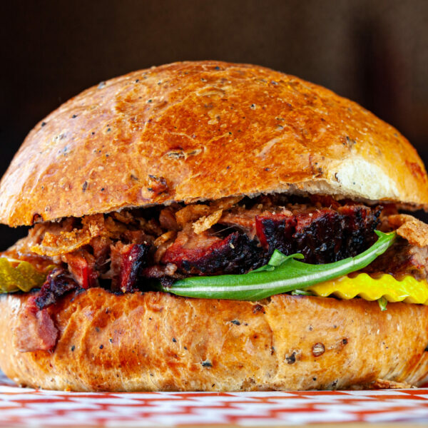 A Prairie Dog Brewing Brewer's Brisket Sandwich with slow-smoked Alberta beef brisket, crispy onions, malt vinegar pickles, Red BBQ sauce, arugula.