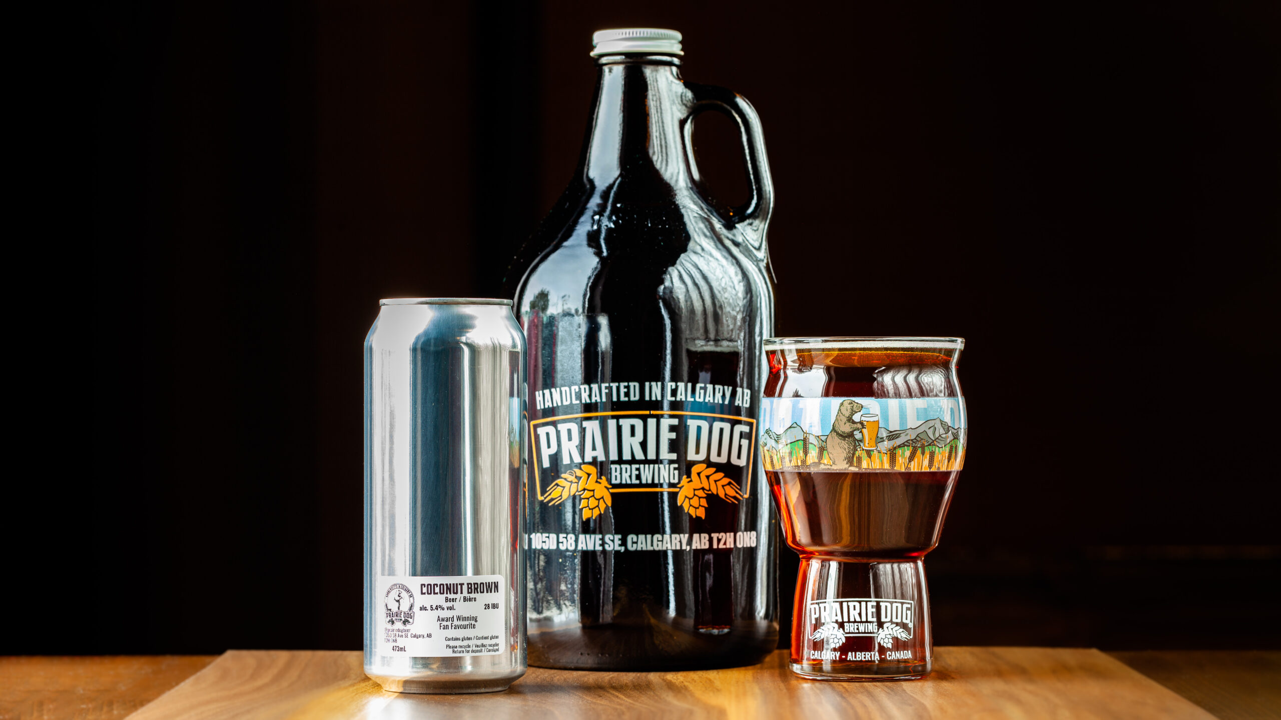 Prairie Dog Brewing's Coconut Brown Ale in three different formats, a 473mL can, a 473mL (16oz) beer glass as draft, and in a 64oz (1.89L) growler jug.