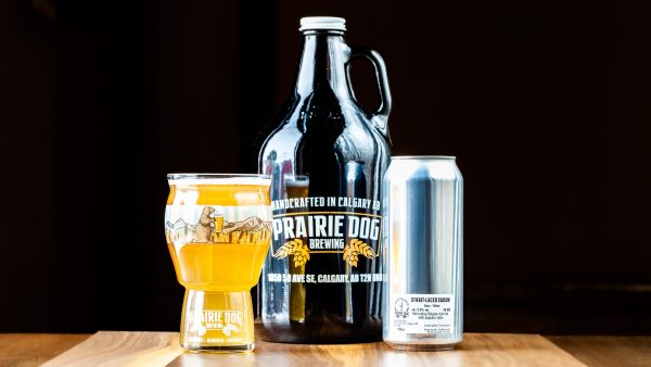 Multiple formats of Prairie Dog Brewing's Strait-Laced Saison, including a 473mL (16oz) draft pour, a 473mL can, and a 64oz growler jug.