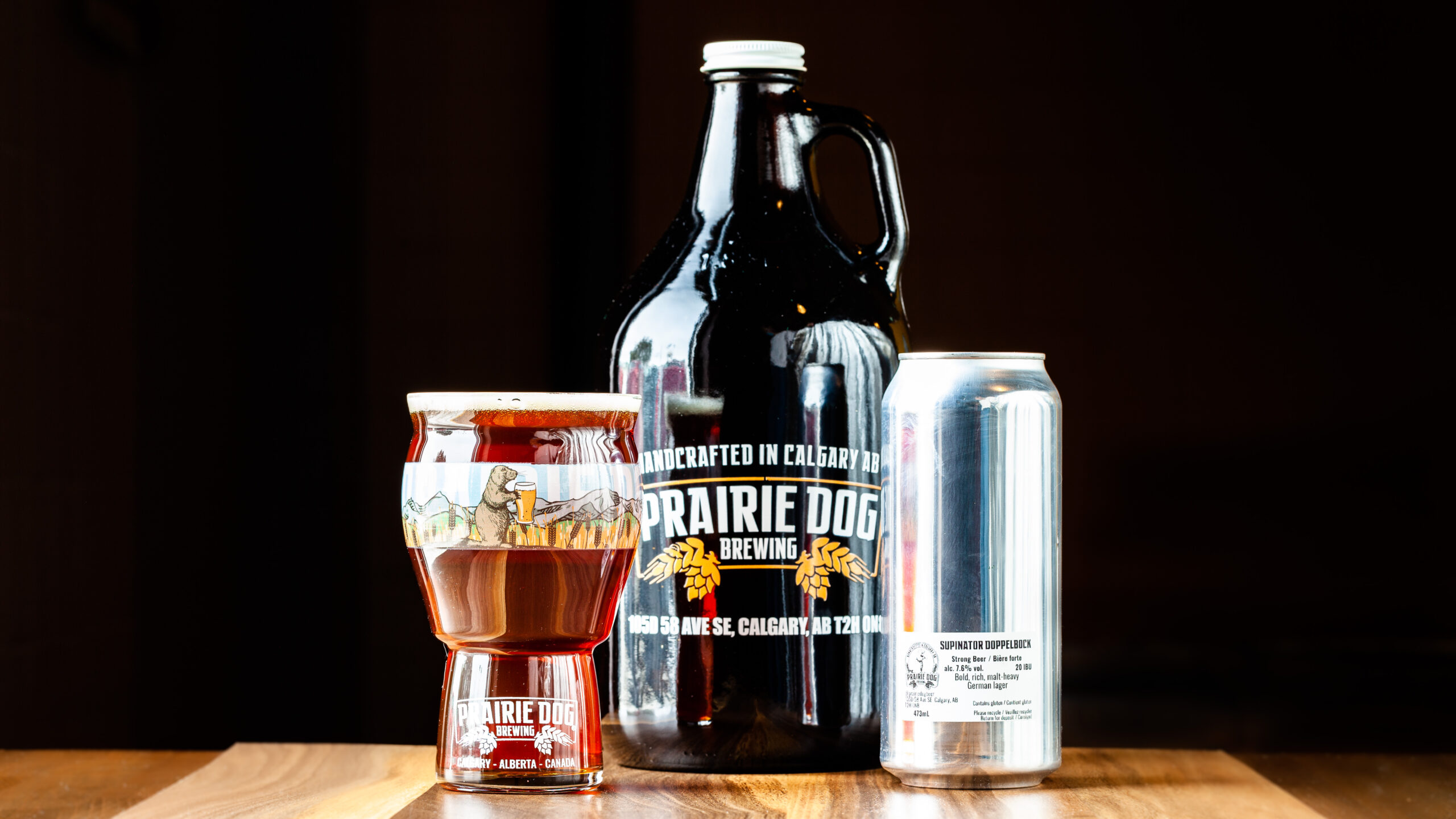 Multiple formats of Prairie Dog Brewing's Supinator Doppelbock, including a 473mL (16oz) draft pour, a 473mL can, and a 64oz growler jug.