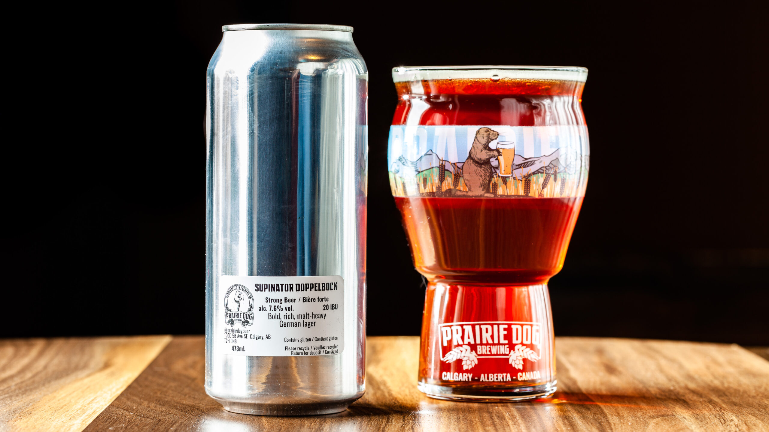 Prairie Dog Brewing's Supinator Doppelbock in a 473mL can beside a branded beer glass filled with the same.