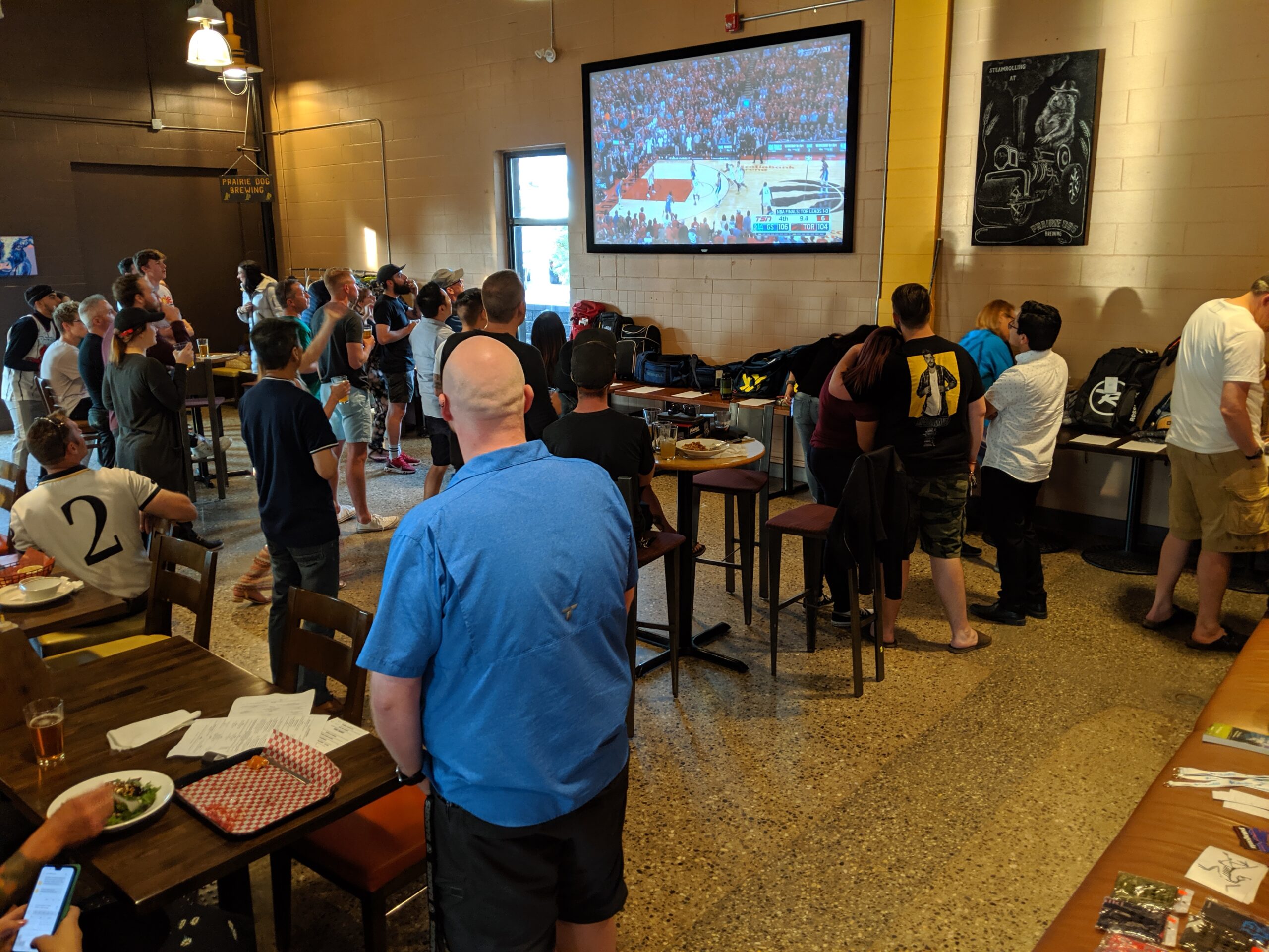 Event guests stand to watch an NBA game on Prairie Dog Brewing's 120" big screen projector.