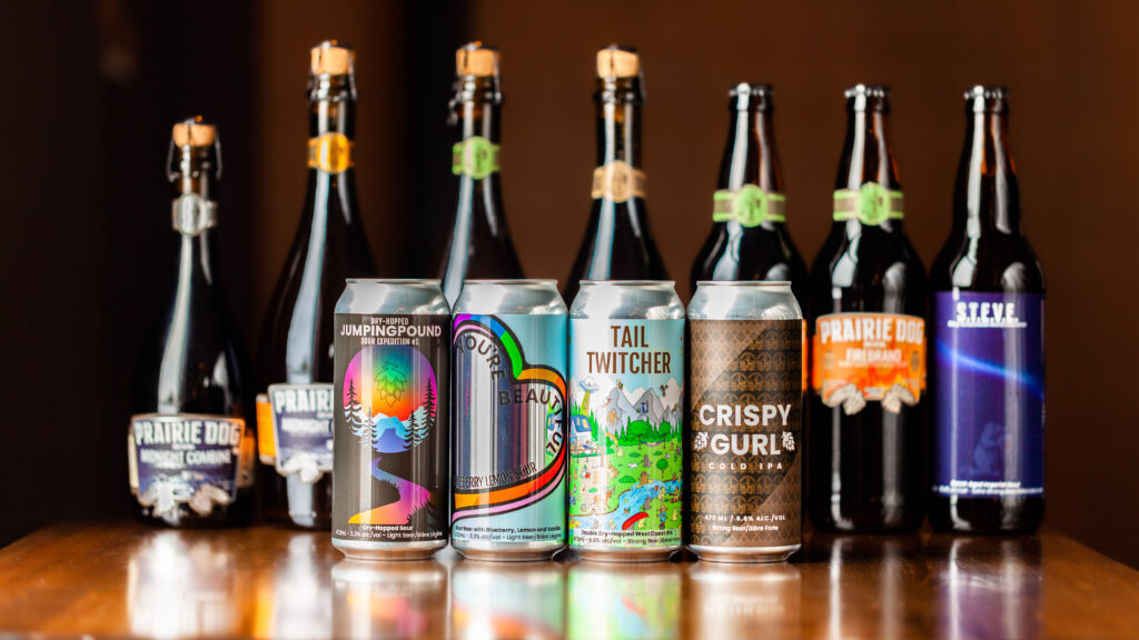 An ensemble shot of Prairie Dog Brewing's retail packaged beer, including special release bottles and cans. Midnight Combine, Firebrand, Zinful, STEVE, Sour Expedition 1, You're Beautiful, Tail Twitcher, Crispy Gurl.