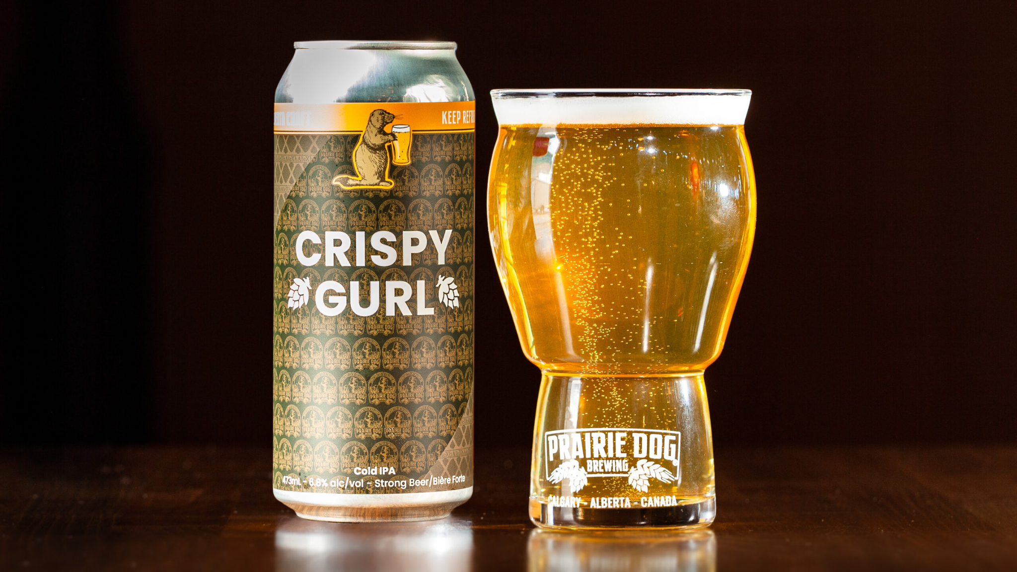 Crispy Gurl v4 Can + Glass Prairie Dog Brewing and XhAle Brew Co. collab beer Crispy Gurl, a Cold IPA, in a 473mL can beside a pour of the same beer in a Prairie Dog Brewing beer glass.