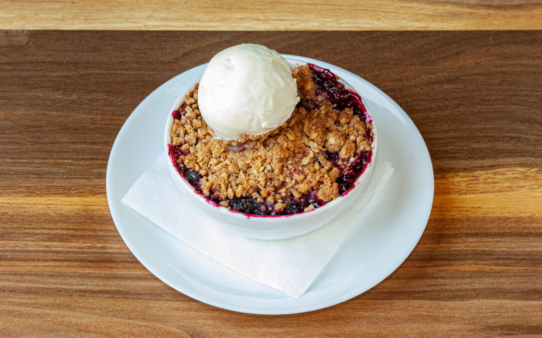 A bowl of Prairie Dog Brewing's Seasonal Fruit Crumble, topped with a scoop of vanilla bean gelato. A part of the Summer Feature Menu for 2023.